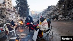 Люди согревается у костра, пока продолжаются поиски выживших после смертоносного землетрясения в Кахраманмараше, Турция, 13 февраля 2023 года.